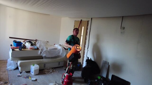 A worker heats a suspended ceiling with a gas heater. Workers are installing a suspended ceiling