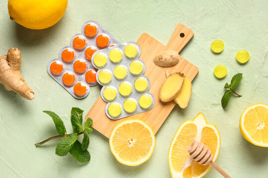 Cough drops in blisters with lemons, mint leaves and ginger root on green background