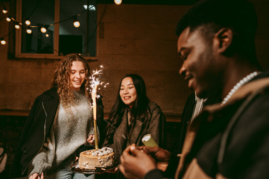 Friends celebrating a birthday indoors with a cake and sparklers in a cozy, festive atmosphere at night