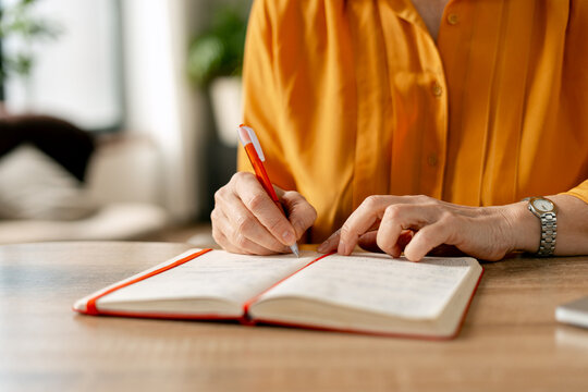 Woman's hands writing notes in an open red journal on a wooden desk