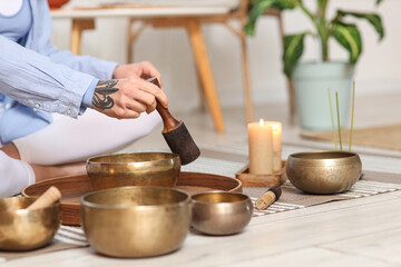 Young woman using Tibetan singing bowls on floor at home, closeup