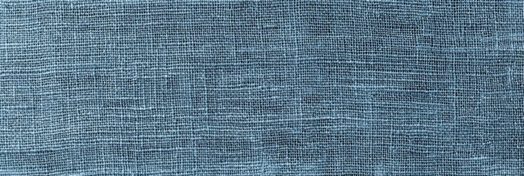 A panoramic view of a dusty blue linen fabric texture showing a detailed coarse weave pattern. The textile surface features interlaced threads creating a rustic and natural look.