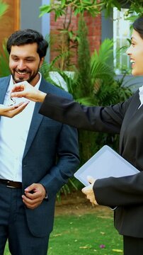 Indian woman real estate agent giving keys of new home to young couple outdoors in a lawn while celebrating their property possession and house purchase during a bright and sunny day.