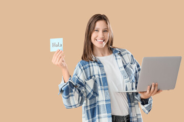 Young woman holding speech bubble with word HOLA and laptop on beige background © Pixel-Shot