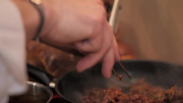 Chef&rsquo;s hands placing meat in frying pan