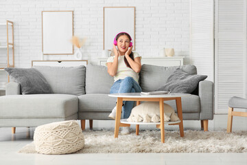 Obraz premium Beautiful young happy Asian woman in headphones listening music on sofa at home