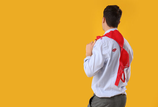 Young man with kiss marks on his shirt and red bra against yellow background
