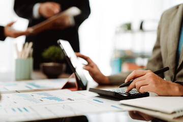 Young colleagues discuss business and analytical price charts using calculators and laptops to calculate financial, tax, accounting, statistics and analytical research ideas. © Dino