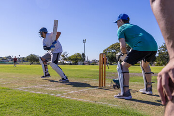 Male cricket players preparing to bat wearing helmet and pads by wooden stumps on grassy pitch © wavebreak3