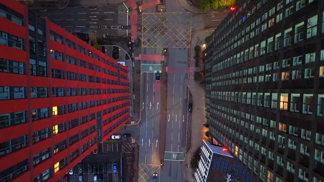 Top-down aerial video capturing the geometry of the red brick and dark glass towers flanking a complex road junction in the early morning in Manchester, UK. 