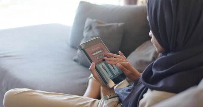 African American woman on sofa opening clothing app, scrolling, saving jacket on tablet, copy space