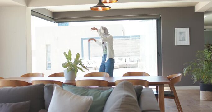 Woman in 20s entering from right pausing at home glass door, dancing to music on headphones