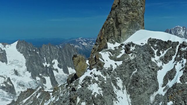 An aerial reveal shot of a dramatic rocky stack peak in the French Alps near Chamonix, capturing the rugged granite texture and vast snowy landscape of the Mont Blanc massif