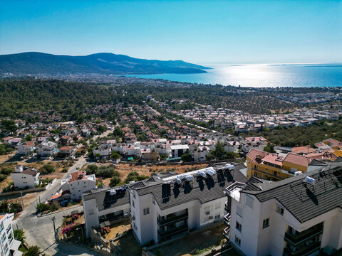 Aerial panoramic view of Didim coastal resort in Turkey, showing the town, a lush forest hill, and the sparkling Aegean Sea under a clear sky.