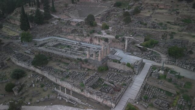 Aerial drone orbit shot around the Temple of Apollo ruins in Delphi, Greece at sunset, showcasing ancient archaeological landmark.