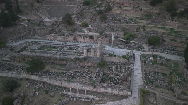 Aerial drone orbit shot around the Temple of Apollo ruins in Delphi, Greece at sunset, showcasing ancient archaeological landmark.