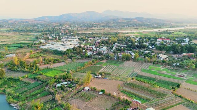 Aerial drone view of Lak Lake in Dak Lak showing rural village, patchwork farmland, green fields, and rolling hills near calm water forming scenic countryside landscape