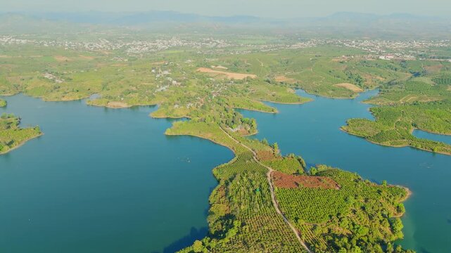 Aerial drone view of Ta Pa Lake in An Giang showing blue water, small islands, green vegetation, and winding road forming scenic natural landscape under clear sky