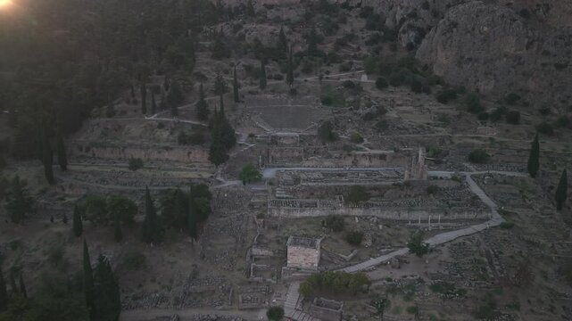 Aerial drone pull back reveal shot of the Temple of Apollo ruins in Delphi, Greece at sunset.