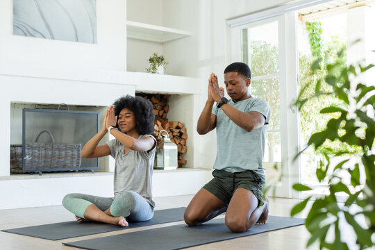African American couple meditating on yoga mats at home by doors prompted by sunlight for calm