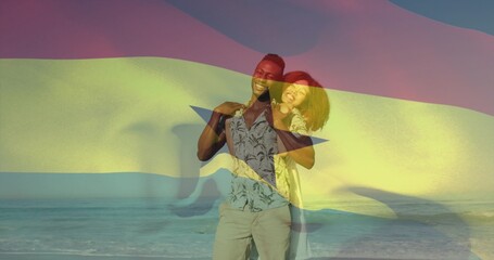 Fototapeta premium Standing couple embracing on beach at sunset, wearing shirt and sundress, Ghana flag overlay