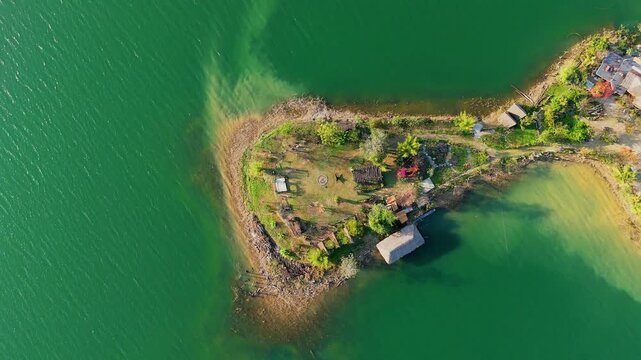 Aerial drone view of Tri An Lake in Vietnam showing small green peninsula, clear water, rocky shoreline, and natural surroundings forming peaceful scenic landscape