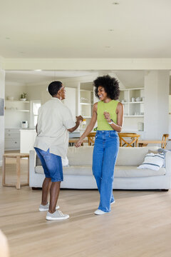 African American couple dancing on hardwood floor in living room with sofa, dining table, shelves
