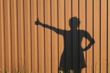 Female shadow with thumb up gesture on brown corrugated metal wall, success and approval concept