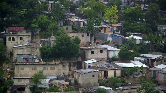 Dense hillside neighborhood in Port-au-Prince, Haiti, showing modest homes, corrugated rooftops, and lush tropical vegetation.
