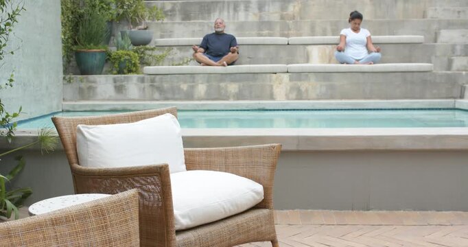 Couple meditating on terraced benches by pool, camera pulling back, doing deep breathing for calm