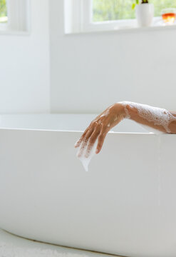 Bath filling starting forearm and hand dripping soap suds while showing calm minimalist bath