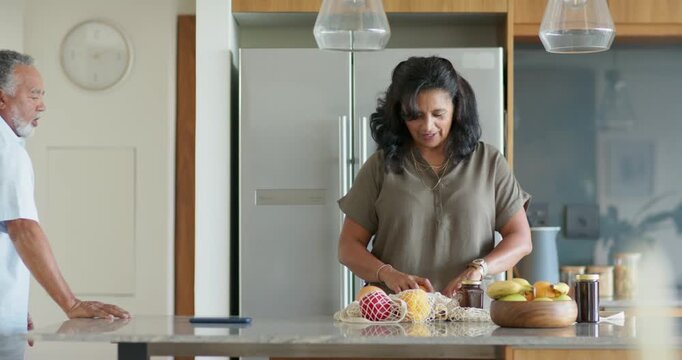 African American couple at kitchen island, woman unpacking mesh bag, urging man handling melon