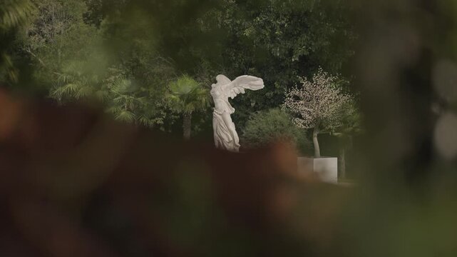 Classic white replica sculpture of the Winged Victory standing in a lush green garden