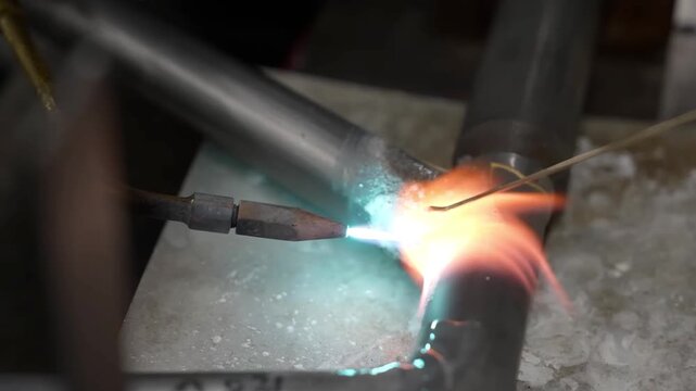 Extreme close up of a bright blue blowtorch flame heating a metal joint during a precision brazing process on a bicycle frame
