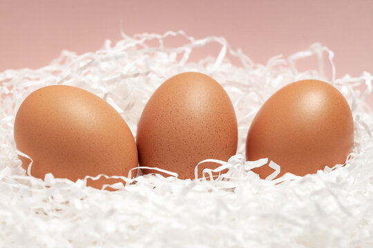 Three brown chicken eggs on pink background for Easter