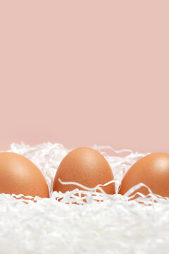 Three brown chicken eggs on pink background for Easter vertical