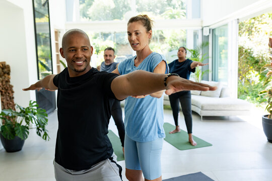 Instructor giving hands-on cue front client holding arms and adjusting posture on yoga mats fitness