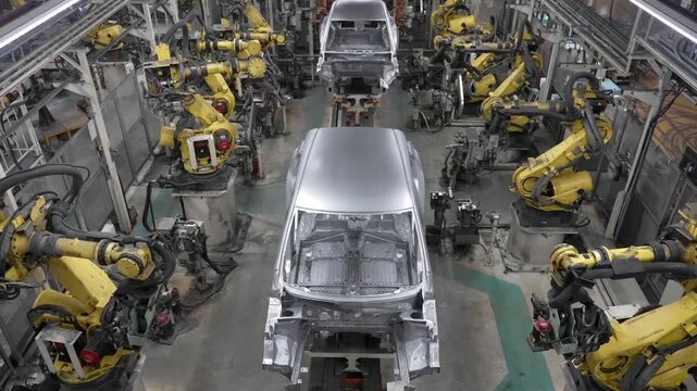 Wide high-angle perspective of an expansive automotive production line featuring rows of yellow robots and car frames in motion