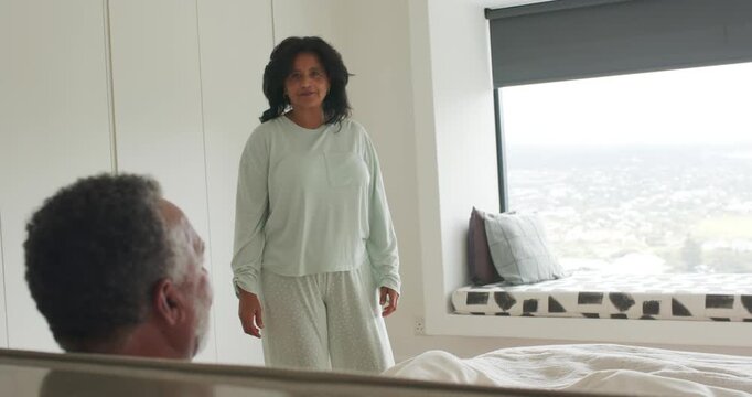 African American couple woman-in-pale-green-pjs walking from right to bed-window-seat, man inviting