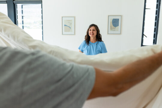 Couple making bed together in bright modern bedroom, holding light-colored duvet and pillows