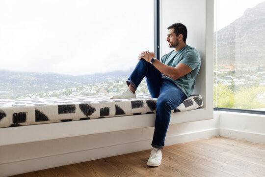 Man sitting on window bench gazing through corner windows at misty valley with watch, copy space