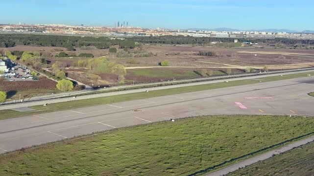 A left side cockpit window view of the shadow of a jet airplane in the final approach to Madrid airport, with Madird city at the background under a blue sky.