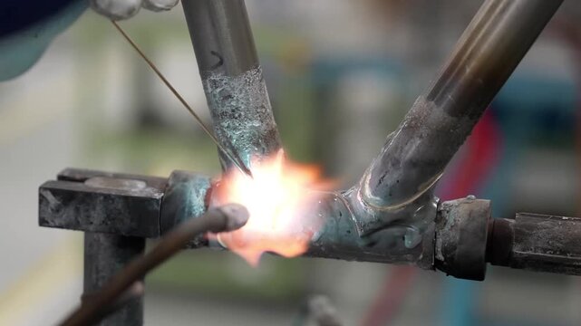 Close up of a professional craftsman manually brazing a lugged bicycle frame joint with a blowtorch and filler rod