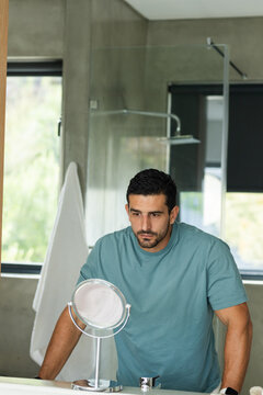 Man leaning on vanity, examining reflection in magnifying mirror at modern bathroom