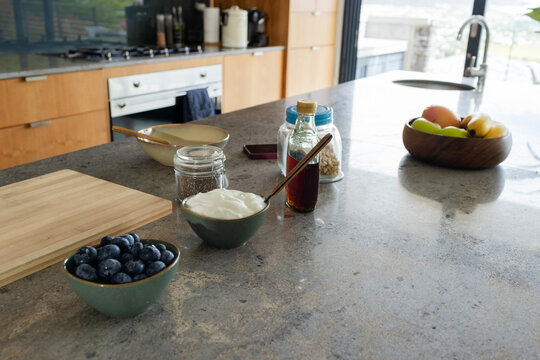 Green ceramic bowl of yogurt sitting centered on stone countertop in kitchen with spoon, smartphone