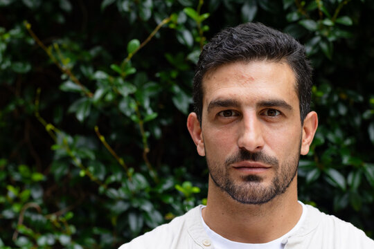 Man posing and gazing at camera in garden, wearing light button shirt and white undershirt