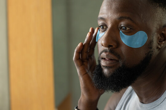 African American man sitting at vanity touching temple wearing tank top and band, blue eye patches