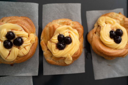 High-angle shot of traditional Italian Zeppole di San Giuseppe, handmade and fresh from the oven. The pastries are resting on a rustic black baking sheet lined with parchment paper, showcasing the gol
