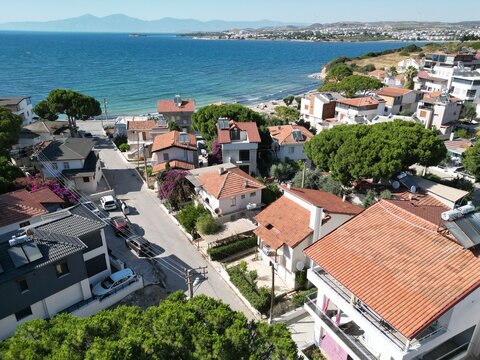 Aerial establishing shot of a Mediterranean coastal neighborhood with terracotta roofs and turquoise Aegean sea at sunny day