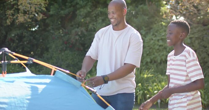 Father and son assembling blue pop-up tent in backyard, adult placing orange pole and teaching son